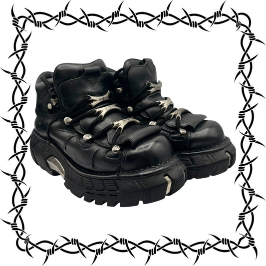 Black leather boots with studs on a white background, framed with barbed wire.