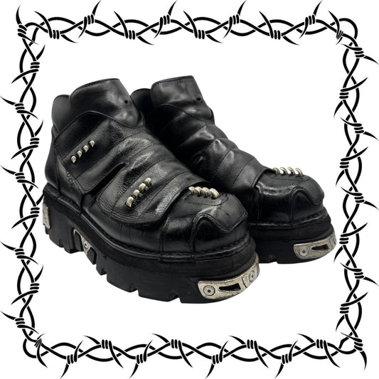 Pair of black leather boots with metallic aaccents on a barbed wire border.